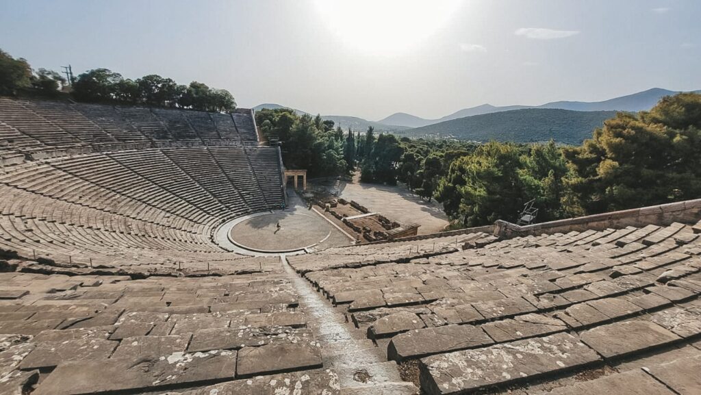 antigo-teatro-epidaurus Teatro antigo de Epidaurus na Grécia, com arquibancadas de pedra em formato semicircular bem preservadas