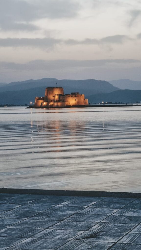 Castelo de Bourtzi iluminado ao entardecer, cercado pelo mar calmo em frente ao porto de Nafplio